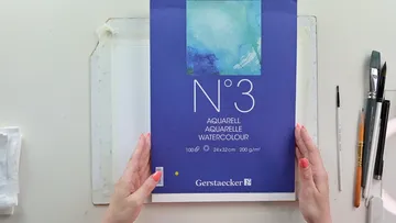 Blauer Block für Aquarellpapier wird gehalten, Kreativumgebung.