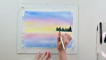 Eine Hand malt eine Landschaft mit Aquarellfarben.