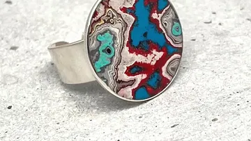 Rings with colorful, patterned stone on a grey background.