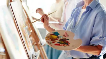 Eine Person malt mit Pinsel und Palette im Atelier.