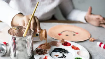 A brush dips into paint while a face is being painted.