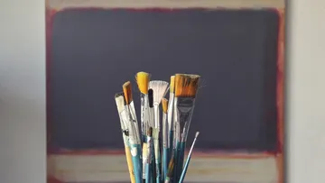 Brushes stand on a table in front of a canvas.