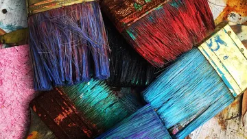 Colourful brushes lay chaotically on a table surface.