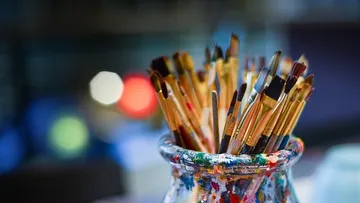 Brushes are stuck in a colorful glass container in a studio.