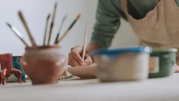 Töpfer handwerkelt mit Pinsel auf einem Tonobjekt.