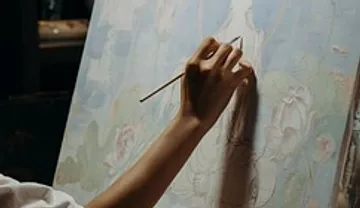 A hand paints carefully on a canvas.