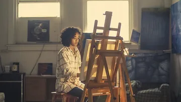 The artist concentrates on an easel in a studio.