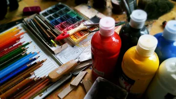 Paints, brushes and pencils lie on a creative table.