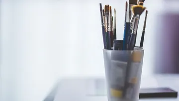 Brushes stand in a transparent container on a table.