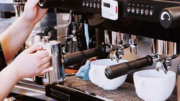 Barista bereitet Milch für Kaffee mit Espressomaschine vor.