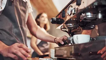 Coffee maker brews coffee while barista works in the cafe.