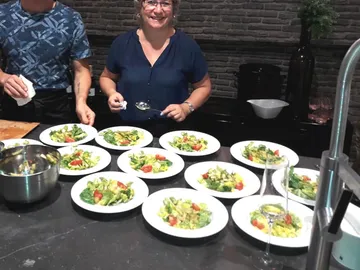 Frau serviert mehrere Salatportionen in einer modernen Küche.