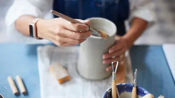 Person painting pottery vase at a table.