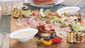 Auf einem Brett liegen Fleisch, Gemüse und eine Sauce.