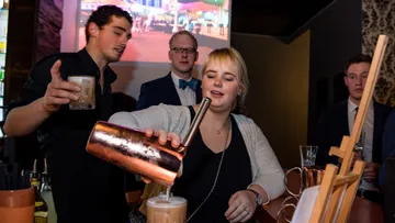 Eine Frau mixt einen Cocktail an einer Bar mit Gästen.