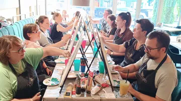 People painting in a group setting at tables.
