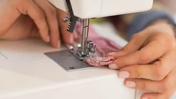 Nähmaschine näht pinken Stoff in einer heimischen Umgebung.