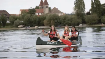Three women are rowing in a canoe on a lake.