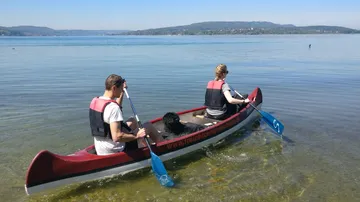 Zwei Personen paddeln in einem Boot auf klarem Wasser.