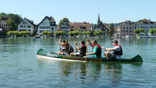 Vier Personen paddeln in einem Kanu auf einem ruhigen Wasser.