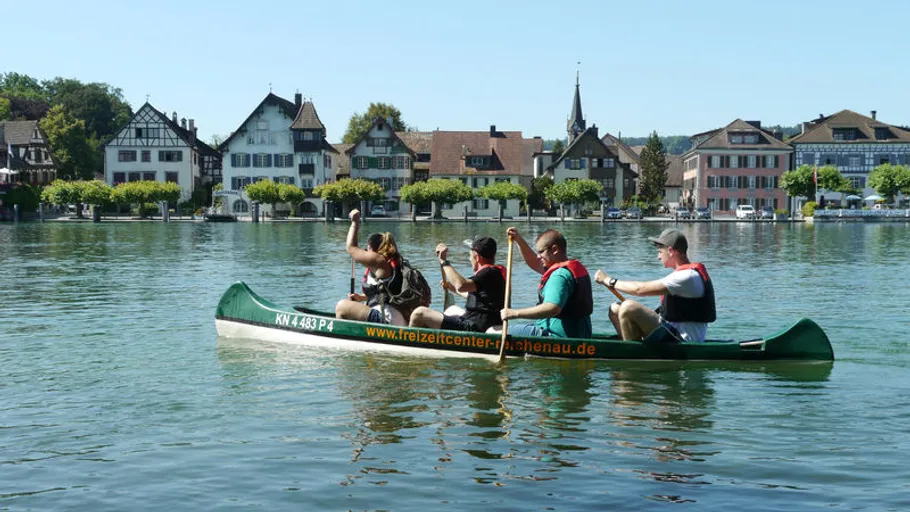 Four people paddle in a canoe on calm water.