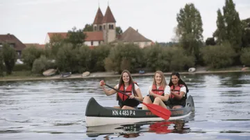 Three women are paddling in a canoe on a body of water.