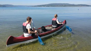 Zwei Personen im Kanu paddeln auf einem ruhigen See.