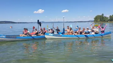 Zwei Kanus fahren mit mehreren Personen auf einem See.