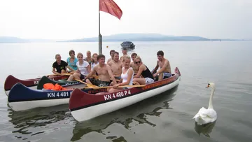Two canoes with young people paddle on a calm lake.