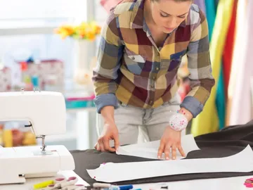 A woman cuts fabric patterns at a table in a sewing room.