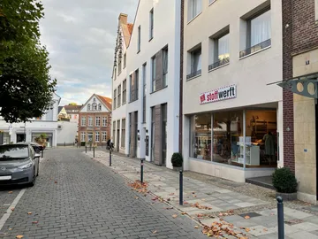 Einkaufsstraße mit einem Stoffladen und herbstlichen Blättern.