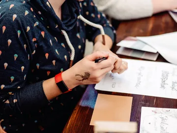 A person writes on paper surrounded by materials.