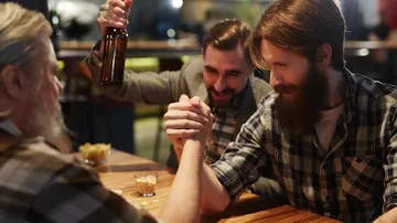 Zwei Männer armdrücken, während einer einen Bierkrug hebt.