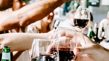 Gläser mit Rotwein werden fröhlich angestoßen. Gesellige Atmosphäre.
