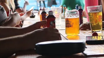 Hände greifen nach Getränken auf einem Holztisch.