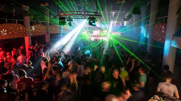 Tanzende Menschen umgeben von bunten Laserlichtern.
