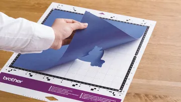 Hand zieht blauen Papierbogen von einer Schneidematte ab.