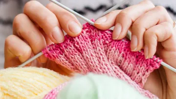 Hands knit pink yarn in a cozy room.