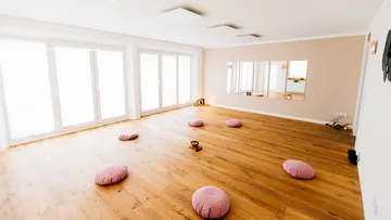 Circles of pillows lie on a wooden floor, the room is bright.