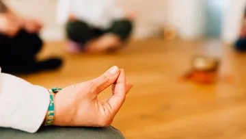 Hand in meditation position surrounded by seated people.