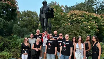 Group of people pose in front of a statue in the park.