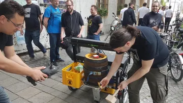 Two men operate a beer keg on a bicycle trailer.