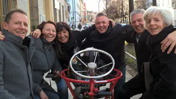 Sechs Personen lächeln und posieren um eine rote Maschine.