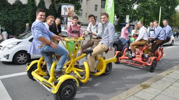 Groups of people ride on colorful, pedal-powered vehicles.