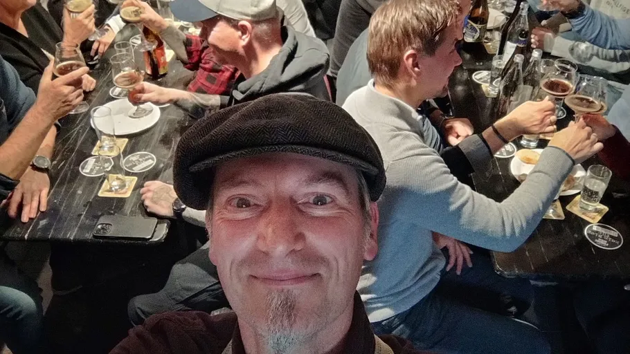 Man taking selfie at crowded beer table.