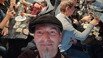 Smiling man in hat at crowded pub with drinks.