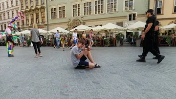 Junge sitzt auf dem Boden und nutzt sein Handy, umgeben von Menschen.