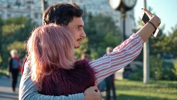 Couple taking a selfie in the park under sunshine.