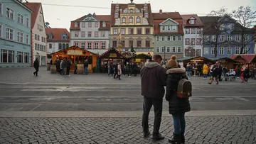 Couple stands in front of a festive market with colorful stalls.