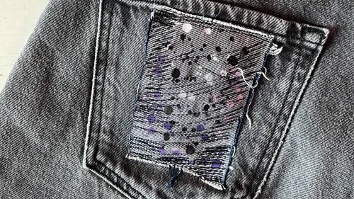 Ein graues Jeansstück zeigt eine gestickte Patches.